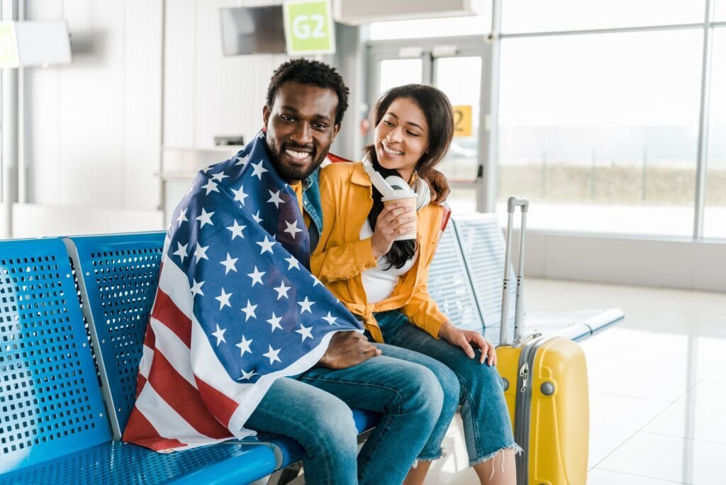 Happy couple with American flag and luggage in airport departure lounge